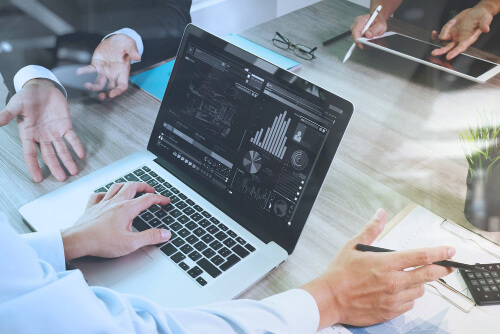 business documents on office table with smart phone and laptop computer and graph financial with social network diagram and three colleagues discussing data in the background x 500-2